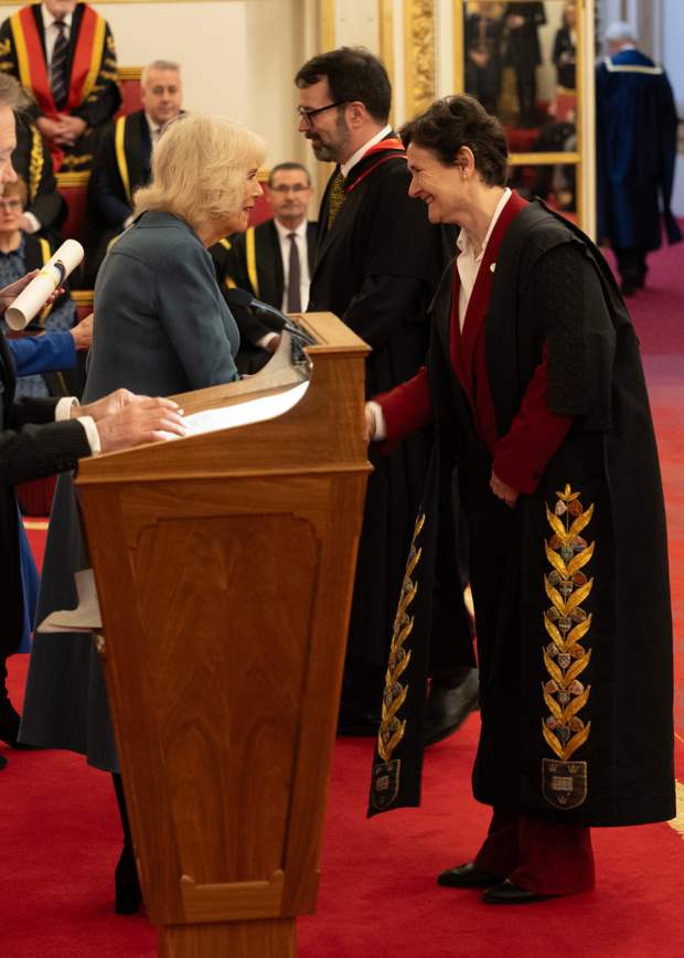 Her Majesty Queen Camilla shakes hands with Professor Irene Tracey. Professor Paul Newman accepts a rolled certificate in the background.